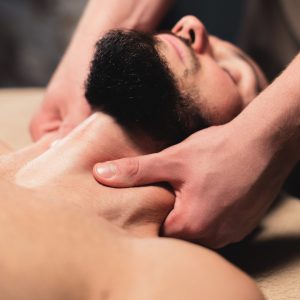 Close-up Professional neck massage to a bearded male athlete in a dark room of a spa massage room.